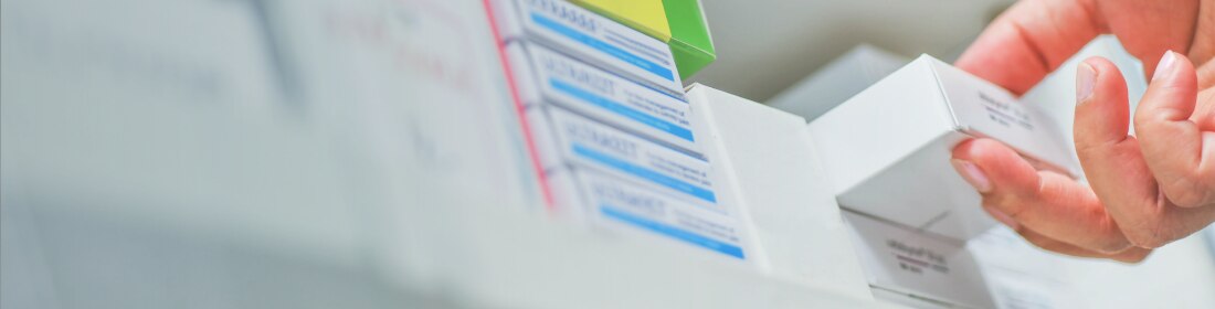 A shelf of pill boxes with someone pulling one box out